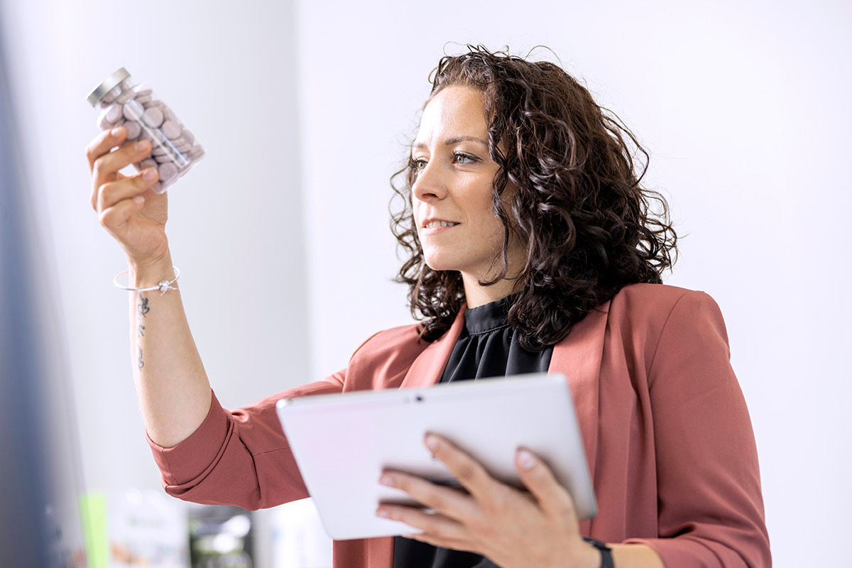 Junge Frau mit dunklen Locken analysiert den Inhalt eines Glases und hält in der anderen Hand ein Klemmbrett