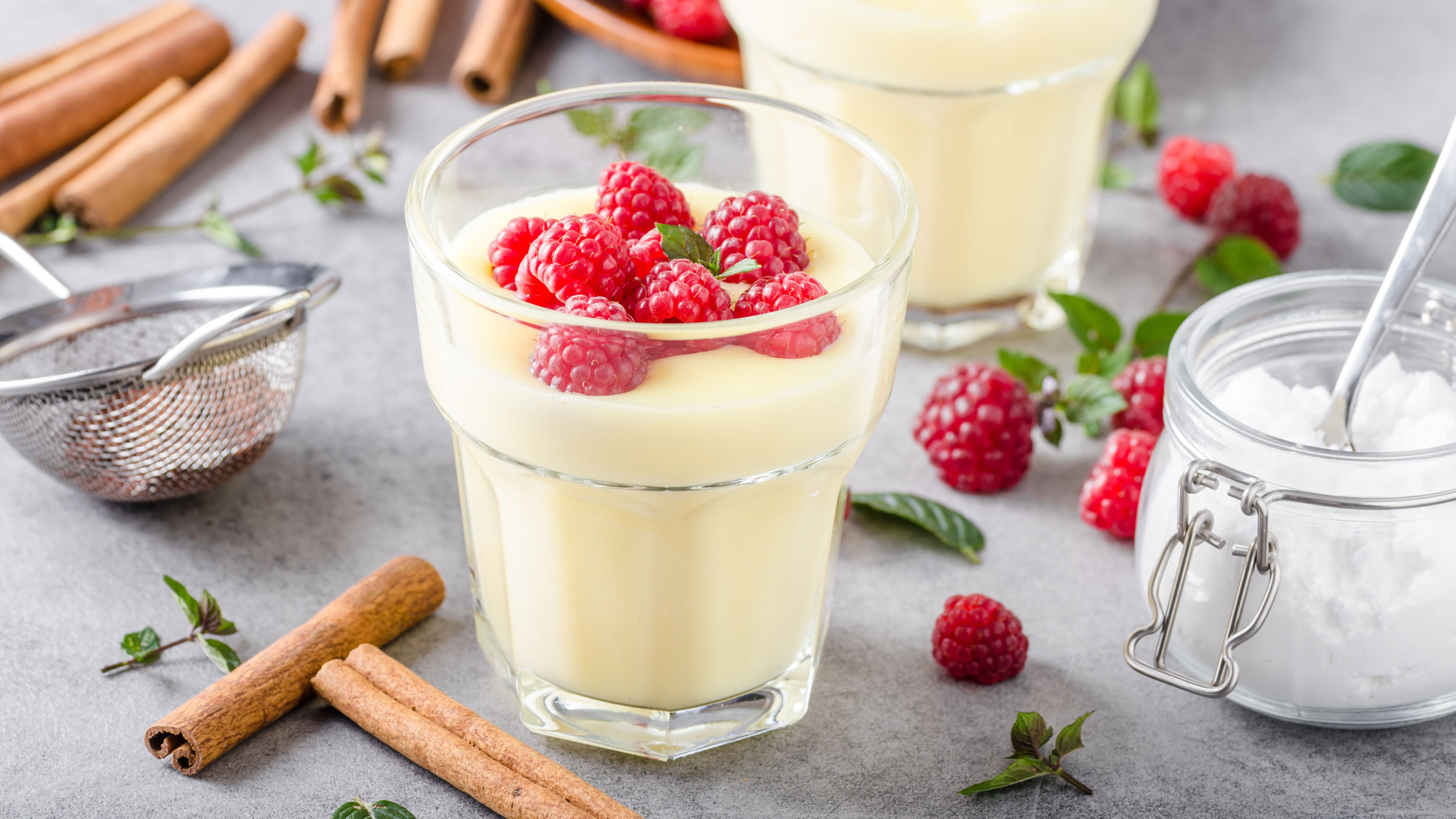 Vanillepudding in einem Glas, dekoriert mit Beere. Im Hintergrund Kochutensilien