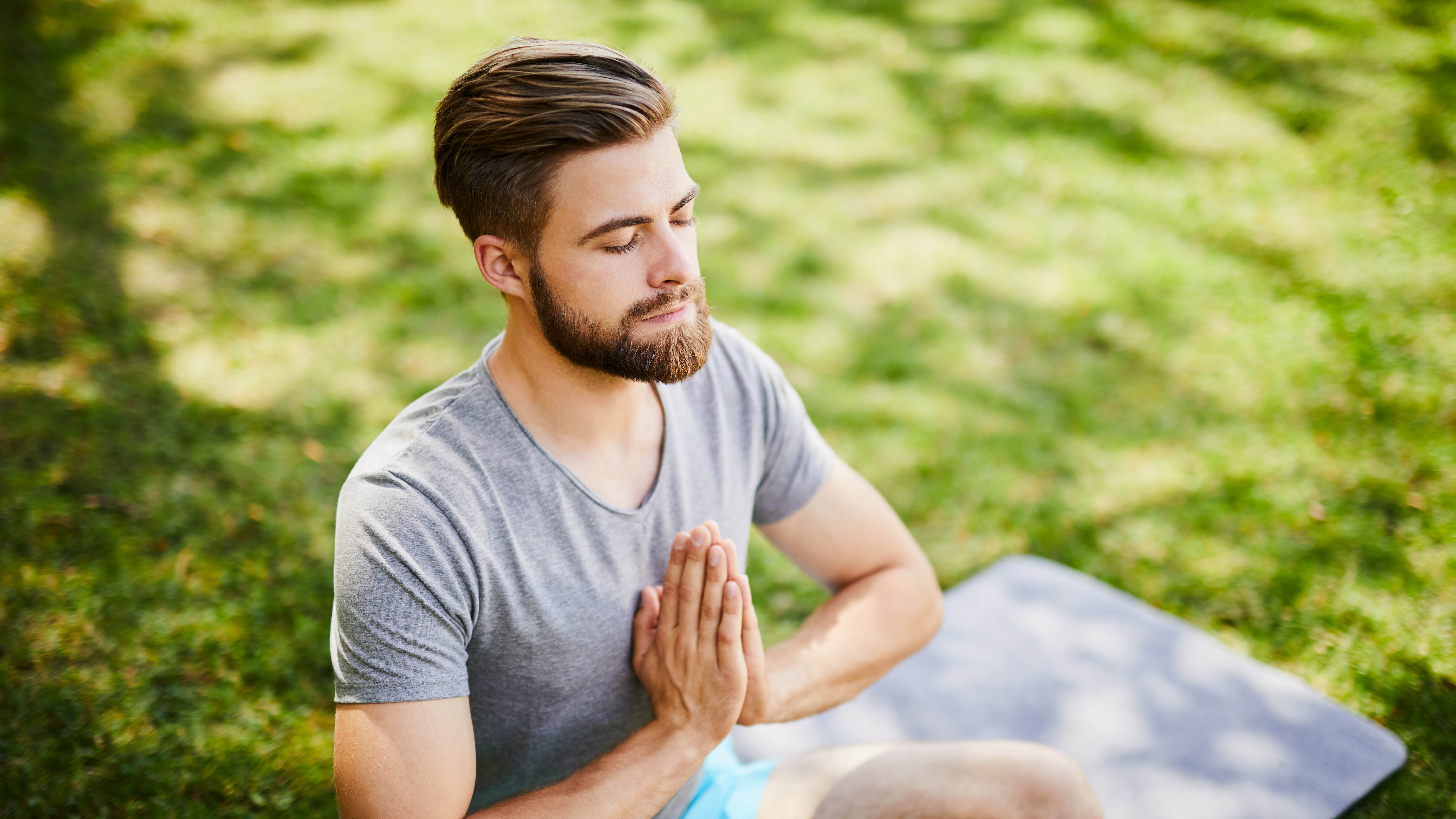 Mann sitzt im Park unter einem Baum und meditiert