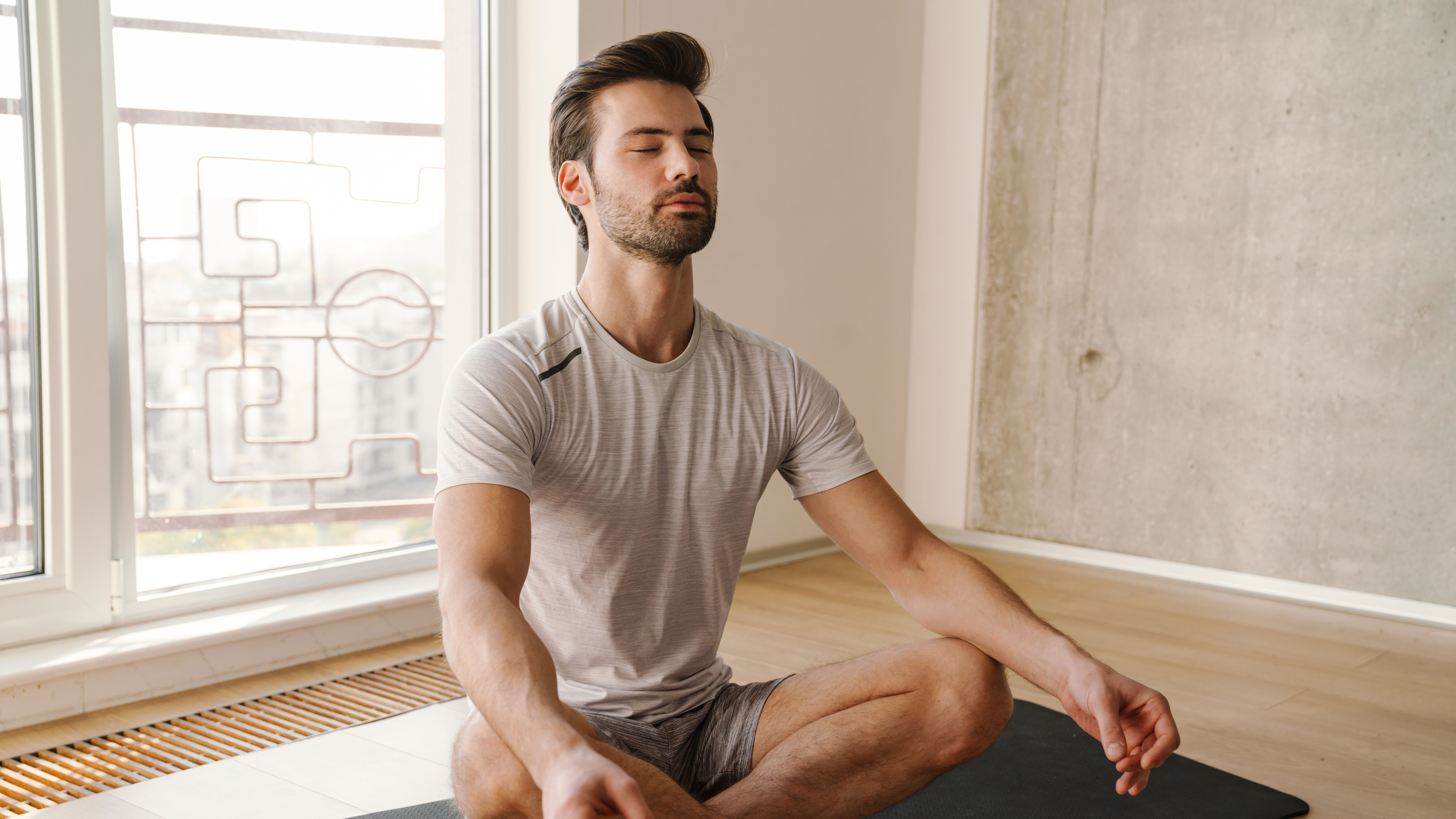 Mann sitzt im Yogasitz und meditiert. Das Bild ist in Grautönen gehalten.