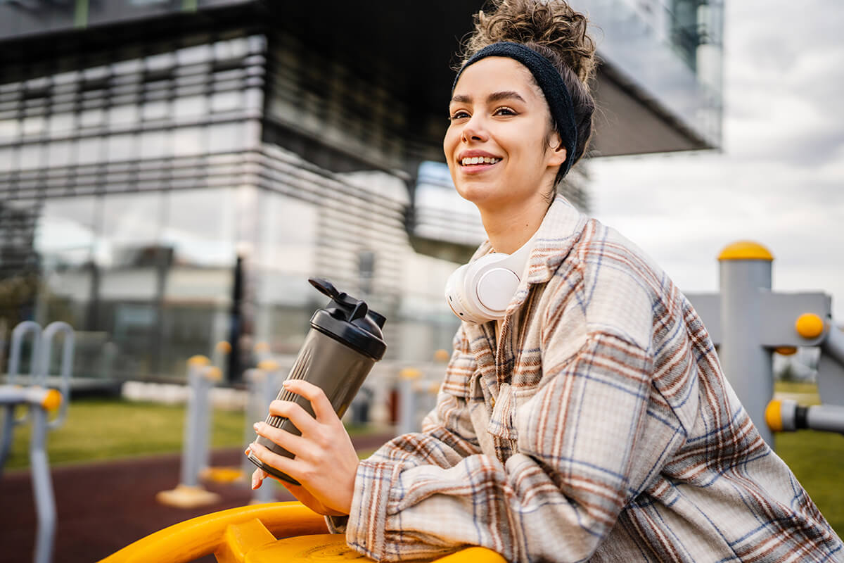 Junge Frau mit Shaker aus dem sie Proteinshake trinkt