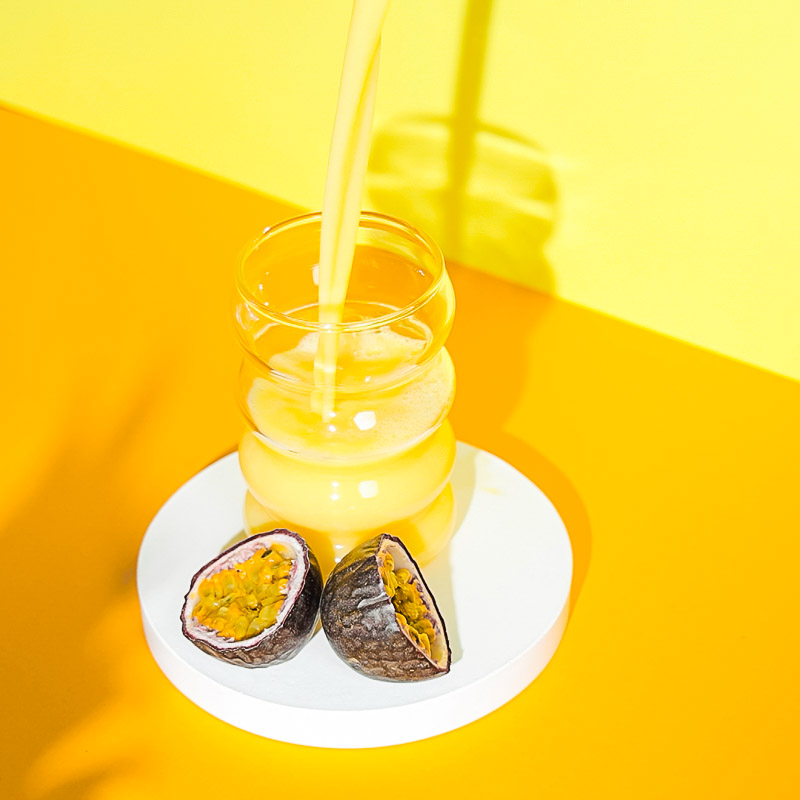 Gelber Hintergrund, davor wird ein gelber Drink ins Glas eingegossen