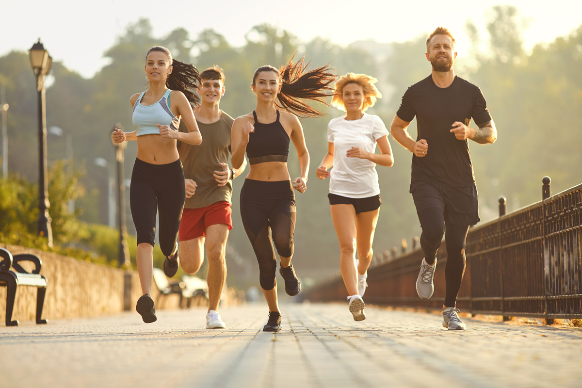 Eine Gruppe von 5 Personen läuft joggend auf die Kamera zu, im Hintergrund ein Park