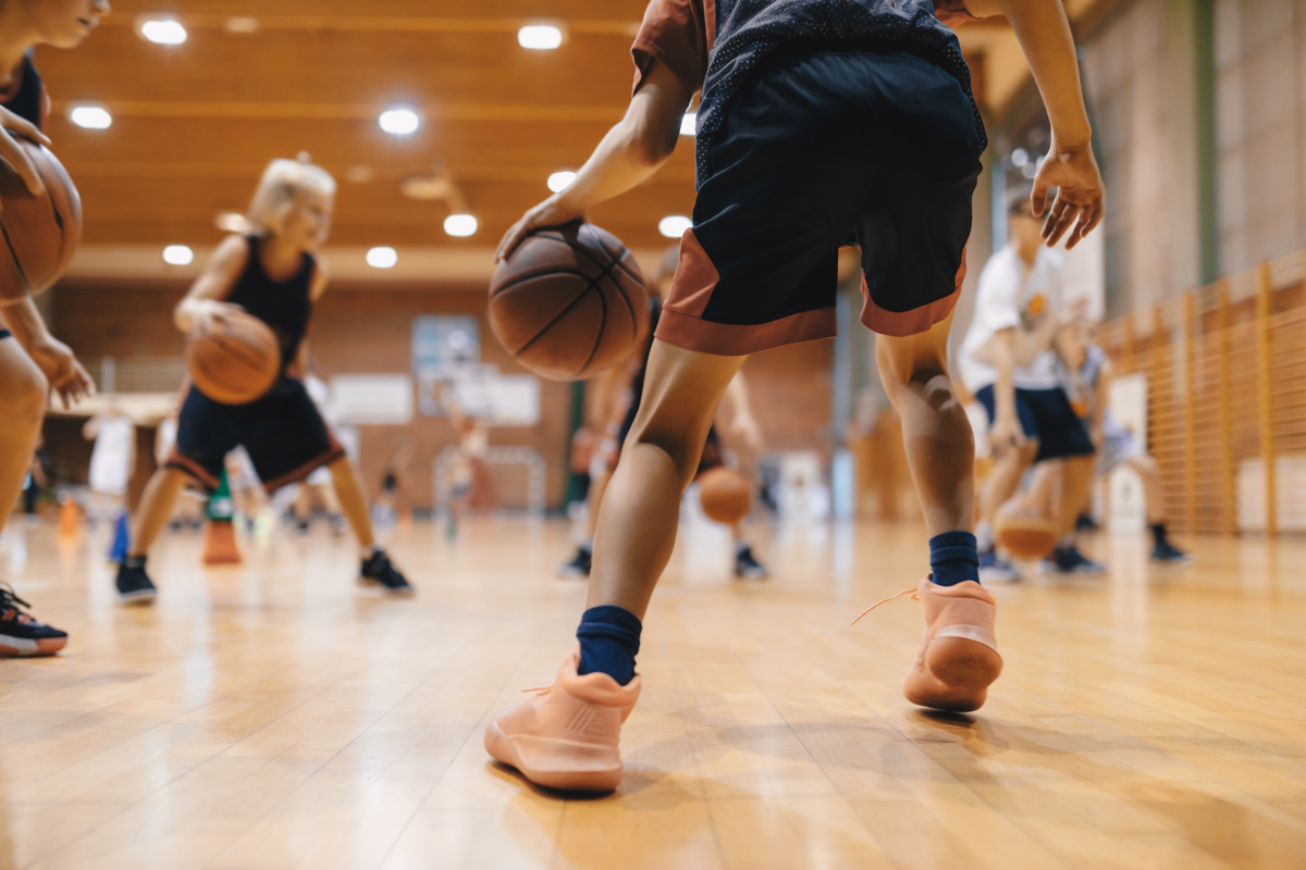 Blick von Hinten auf die Beine eines jungen Basketballspielers, der mit dem Ball drippelt