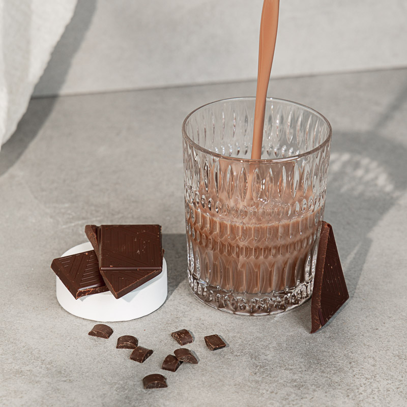 Recovery Drink Schokolade wird in ein Glas eingegossen, daneben liegt Schokolade