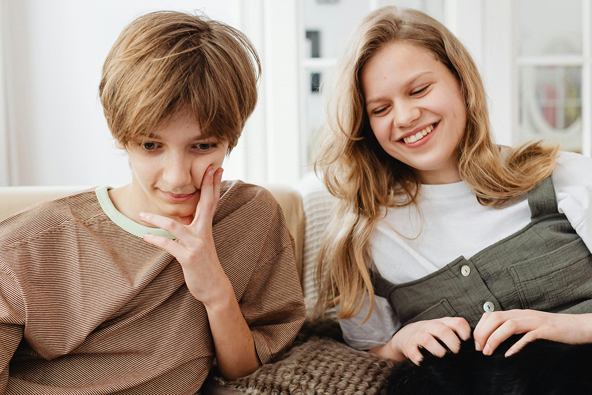 Zwei Jugendliche sitzen gemeinsam auf der Couch und blicken ins Handy