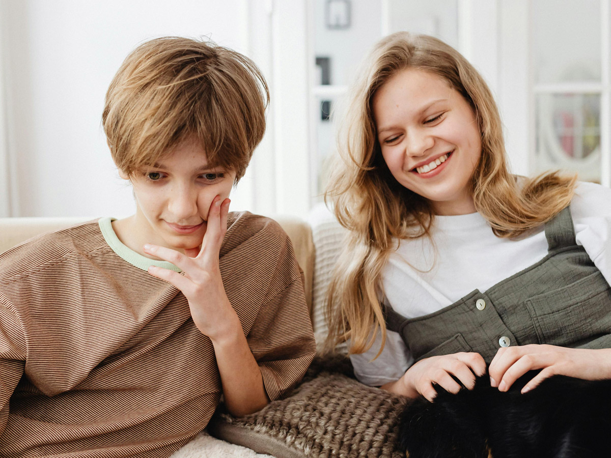 Zwei Jugendliche sitzen gemeinsam auf der Couch und blicken ins Handy