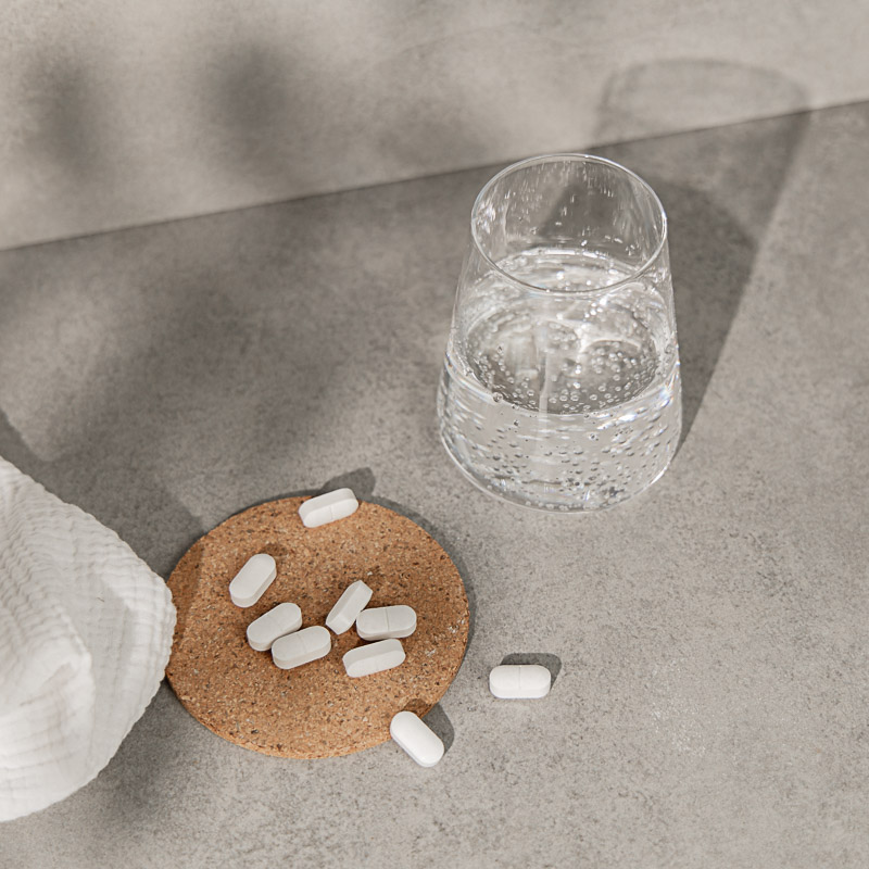 Melatonin Tabletten auf einem Korkuntersetzer, daneben ein Glas Wasser