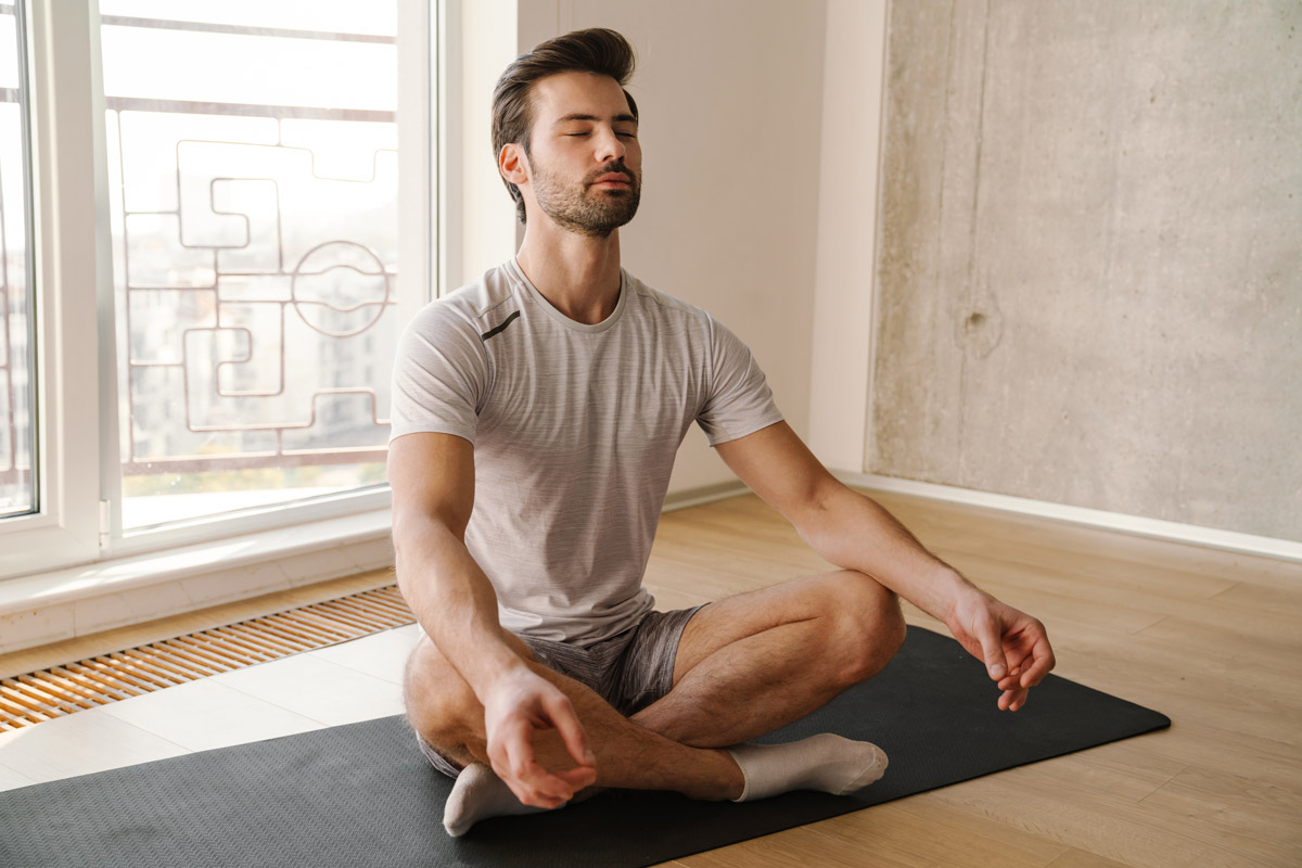 Mann sitzt im Schneidersitz auf einer Yogamatte und entspannt