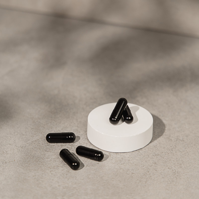 Melatonin Kapseln als natürliche Einschlafhilfe. Schwarze Kapseln auf weißem Podest